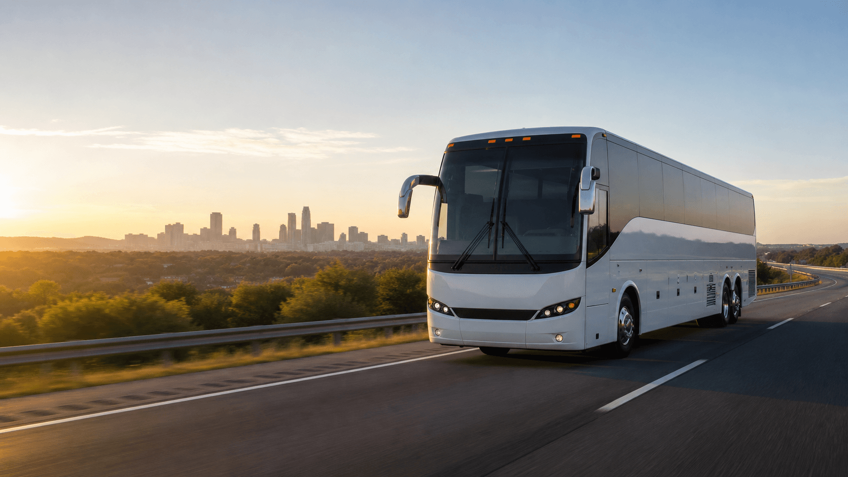 A modern charter coach traveling toward a city at sunrise